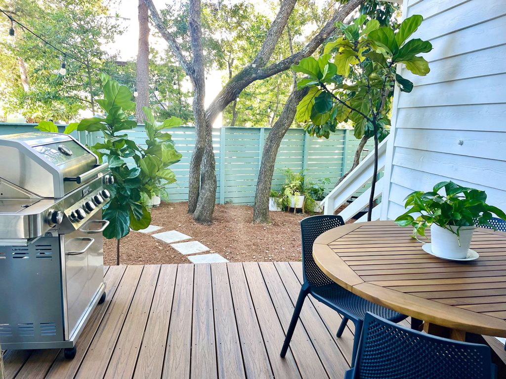 View from cover patio with grill and table overlooking greenery in yard