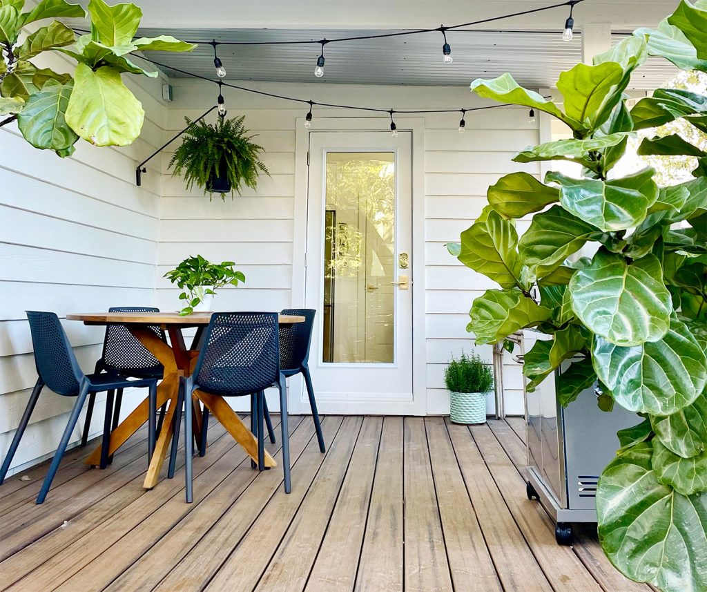 Covered kitchen porch with round dining table string lights hanging fern and grill