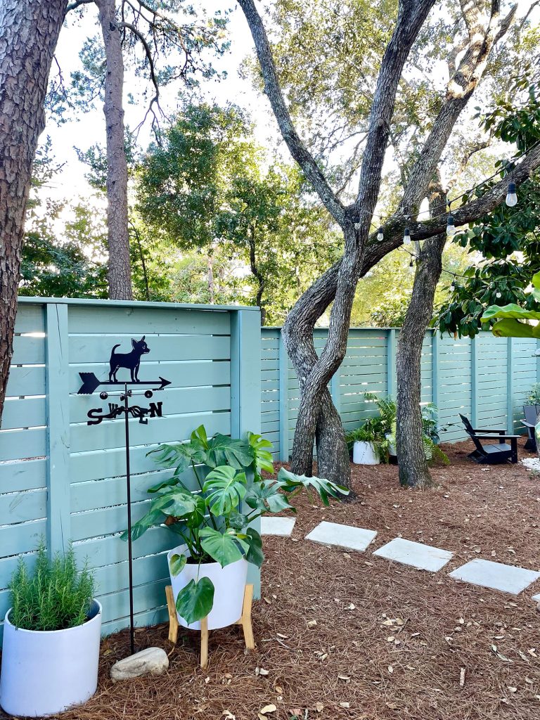 After photo of firepit area with green fence potted plants and chihuahua weathervane