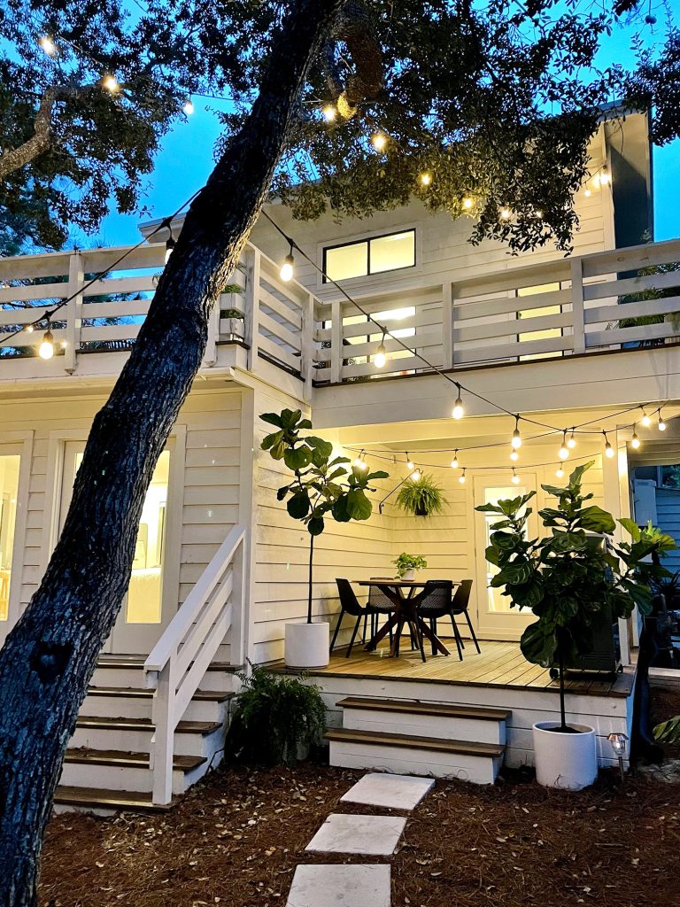 Night photo of porch area with string lights and glowing lights in house