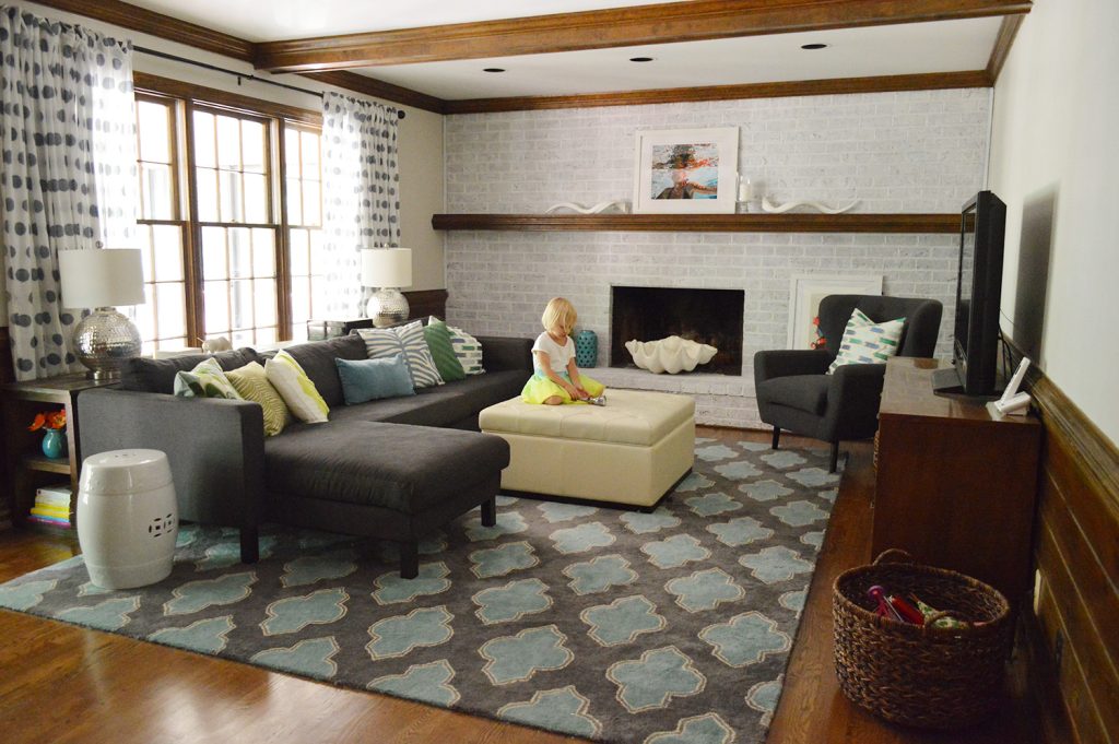 stylish and colorful living room with navy blue furniture, graphic pillows and rug, wood beams, and whitewash brick fireplace wall