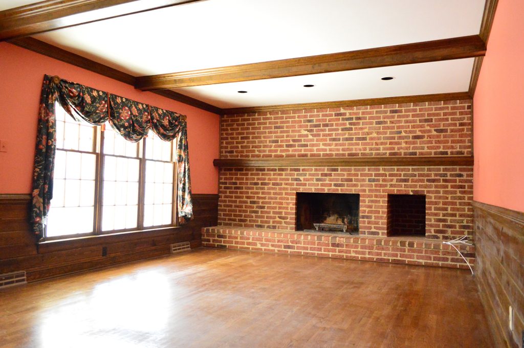 dated 1980s living room with dark brick wall, wood beams, and red salmon colored walls
