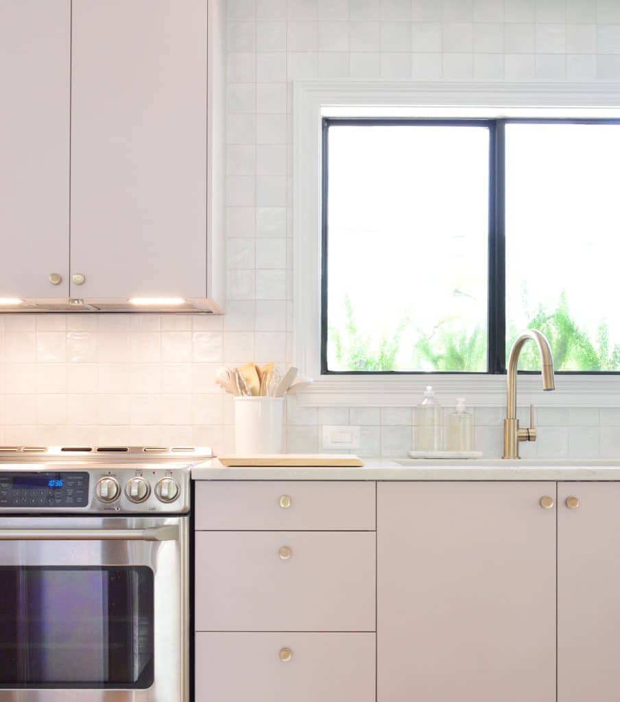 Light on under hidden range hood in beach kitchen against zellige tile