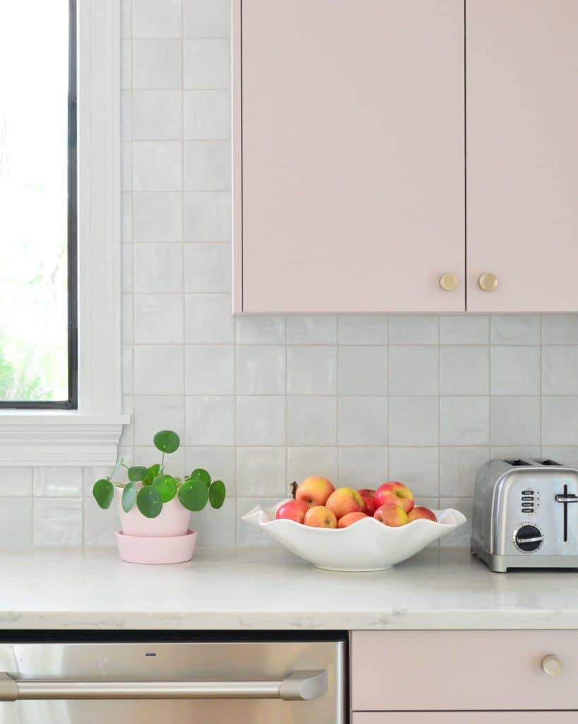 Square Tile Backsplash With Mauve Pink Painted Cabinets And Fruit Bowl