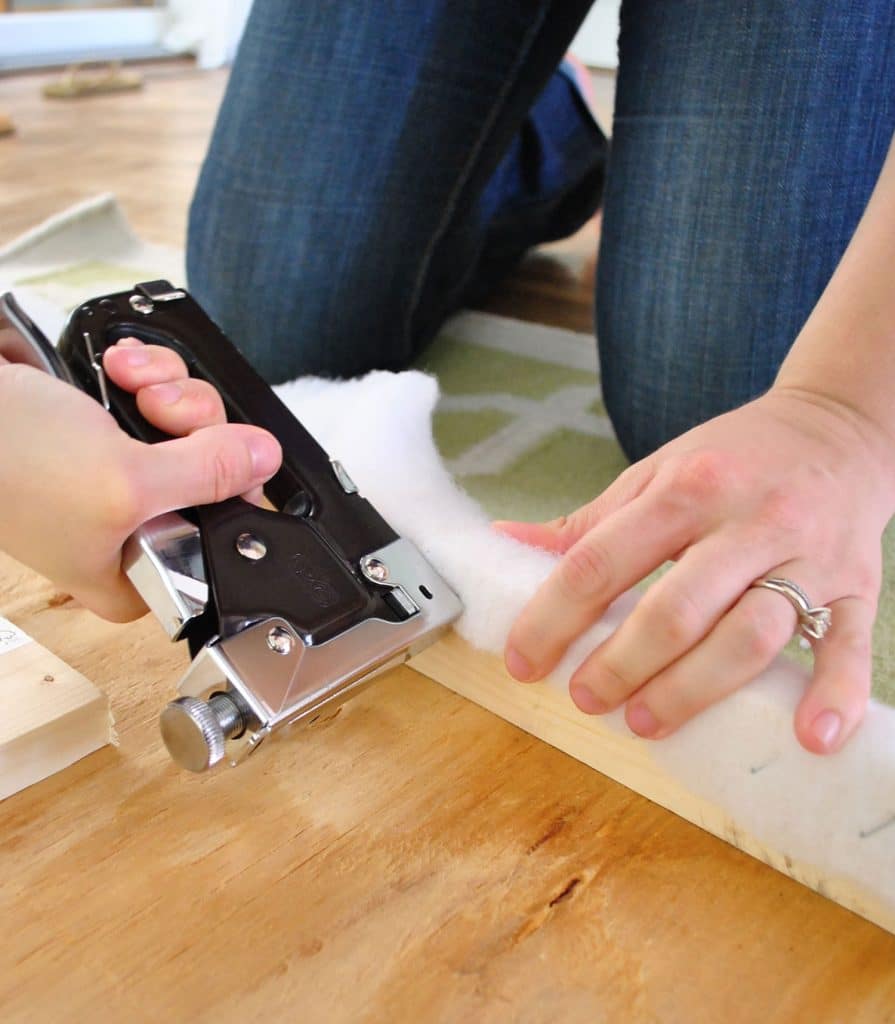 Usando a pistola de grampos para fixar o enchimento na parte de trás da cabeceira de tecido estofado DIY