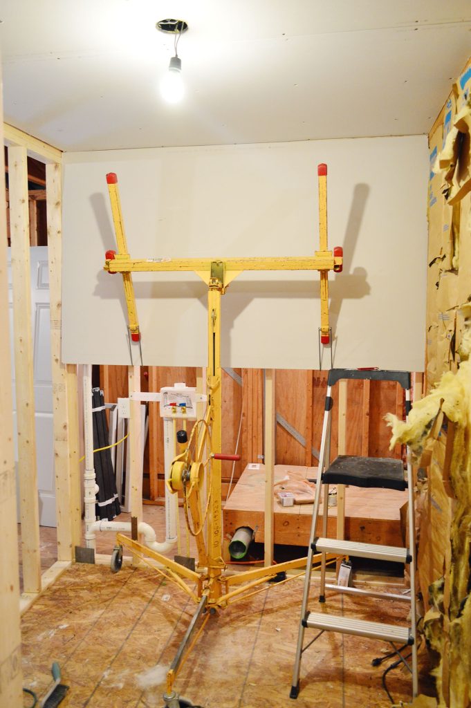 drywall lift holding sheetrock panel in place against wall