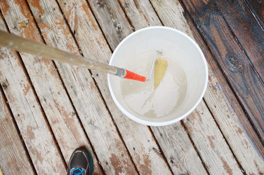 Dipping paint roller into bucket of deck stain stripper