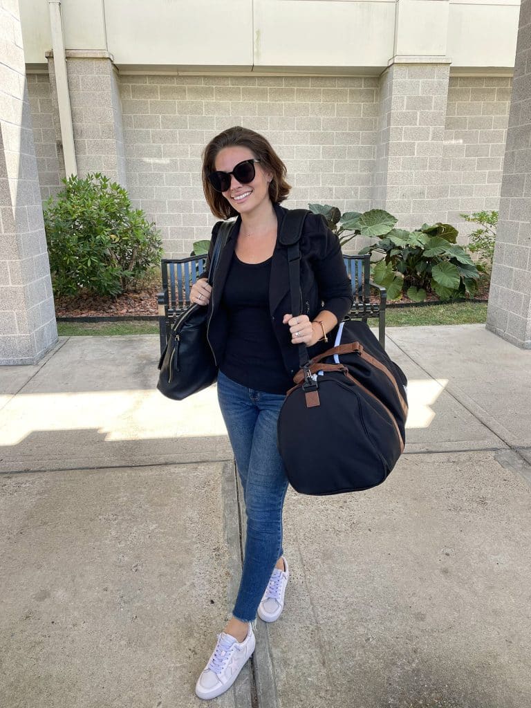 Sherry with purse and duffel bag at airport with black jacket and black tank top and jeans